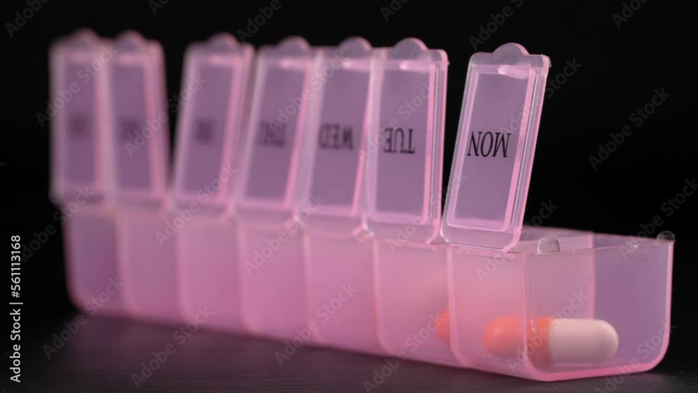 Woman's hand puts pills for week in pill dispenser. Concept of health care and medicines. course of treatment for week. . Storing scheduled doses of medications in box. Woman's hand puts pills for week in pill dispenser. Concept of health care and medicines. course of treatment for week. . Storing scheduled doses of medications in box.