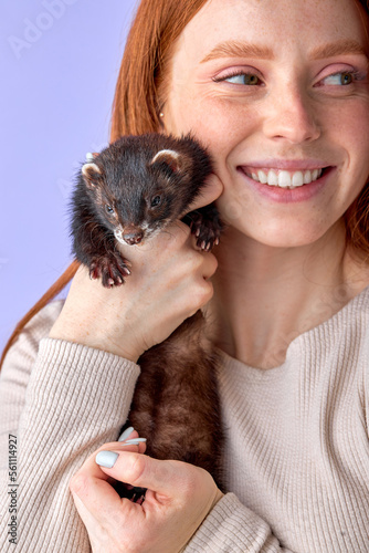 Photography Happy young woman holding ferret isolated on purple studio background, good-looking redhead lady in casual wear posing at camera with animal, portrait