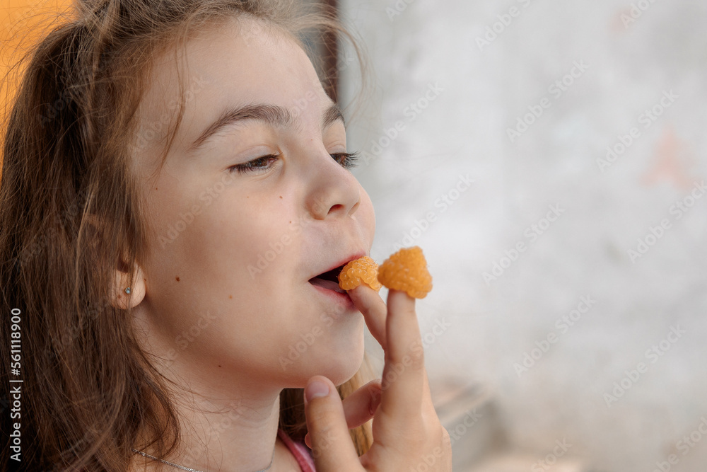 Young girl is holding yellow raspberries on her fingers and tasting. High quality photo Young girl is holding yellow raspberries on her fingers and tasting. High quality photo