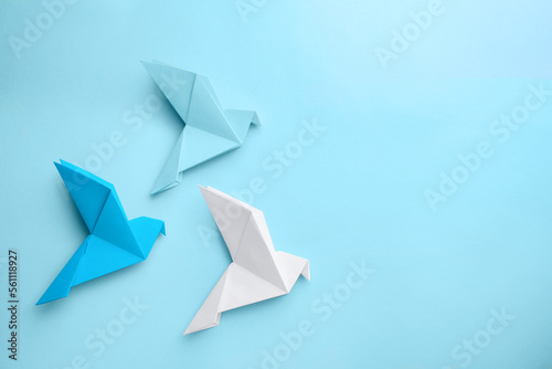 Origami art. Colorful handmade paper birds on light blue background  flat lay. Space for text