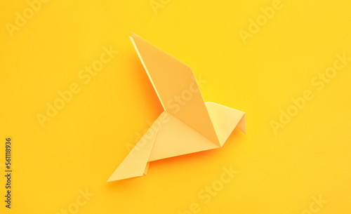 Origami art. Beautiful handmade paper bird on yellow background  top view