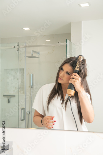Brunnette woman in front of a mirror styling her hair