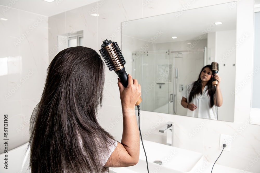 Girl looking at the mirror using a hair dryer brush