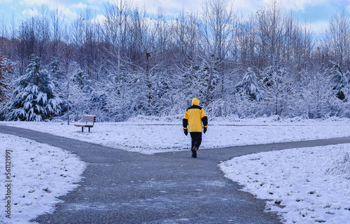 Man in yellow jacket walking in Midwestern city park in snowfall