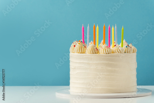 Birthday cake with white cream cheese frosting decorated with multicolored lit candles on a blue background. Happy Birthday concept. .Tradition of making a wish while blowing out candles on a cake