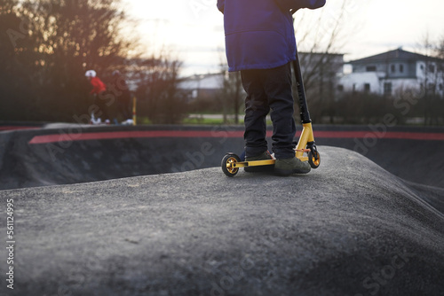 Принти на полотні kid with golden stunt scooter stands on elevation in modern asphalted pump track park