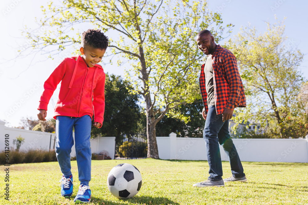 Happy african american father and son playing football in their ...