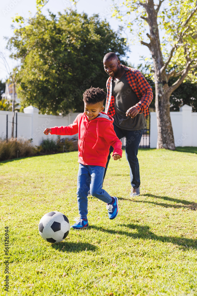 Happy african american father and son playing football in their ...