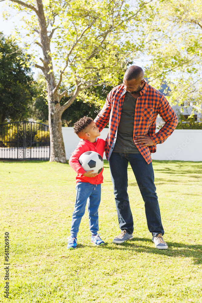Happy african american father and son playing football in their ...