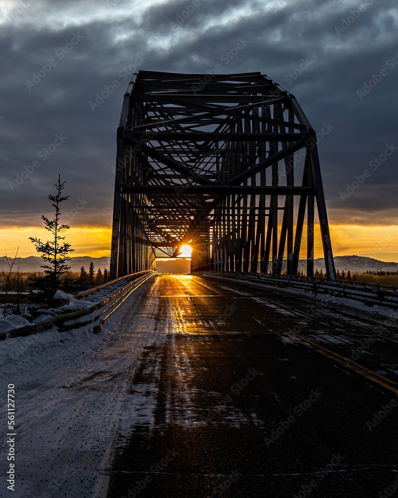 sunrise in Alaska sun shining through old iron suspension bridge on road