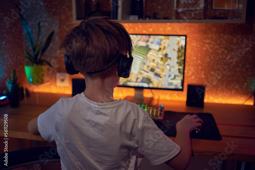 Fotografie Hands of teenage gamer boy playing video games on computer in dark room using ba