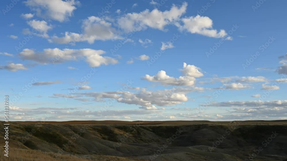 Time lapse of white clouds moving through a blue sky above a badland prairie setting with the sunlight moving on the hills.
Time lapse of white clouds moving through a blue sky above a badland prairie setting with the sunlight moving on the hills.