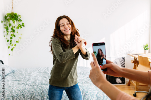Young female friends having fun recording video reels with mobile phone for social media on bedroom. Millennial teenage girls sharing challenge dance on network app. Teen trends lifestyle concept