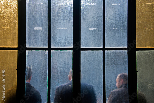 Three men behind colored glass panels waiting for train at station in Porto, Portugal. photo