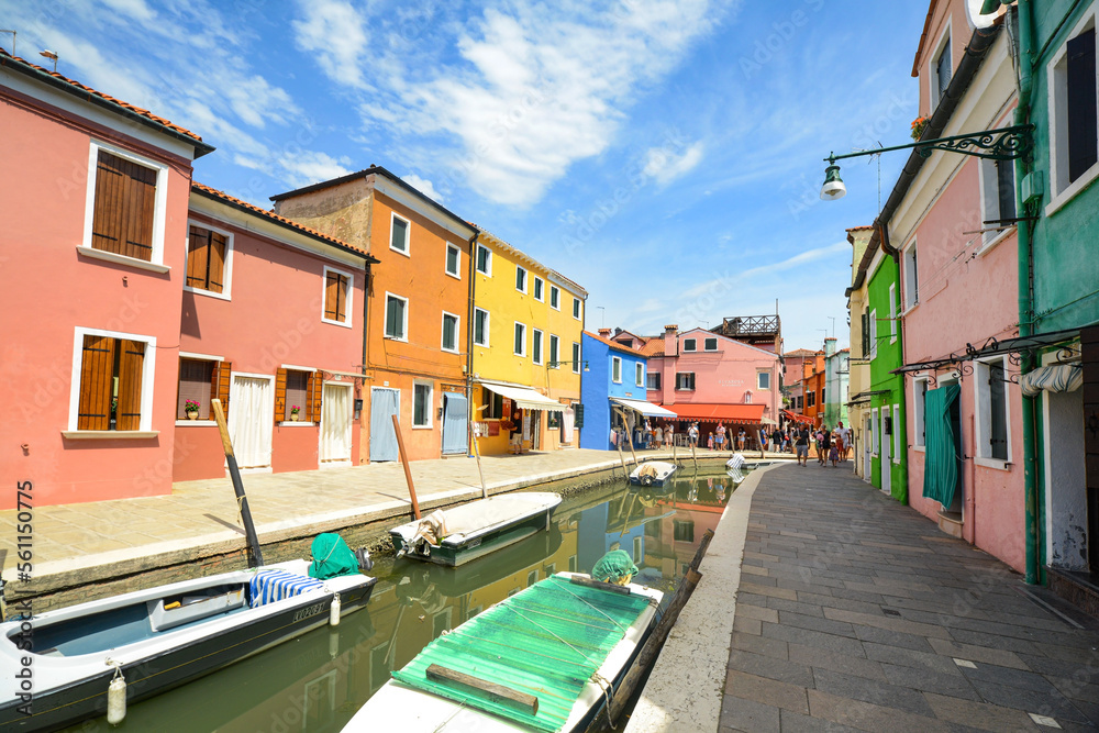 Tourists among the sovereign shops on the main street of burano Island,  Colorful houses on the canal. Venice, Italy.