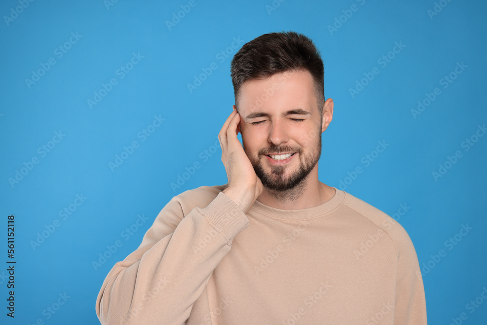Young man suffering from ear pain on light blue background