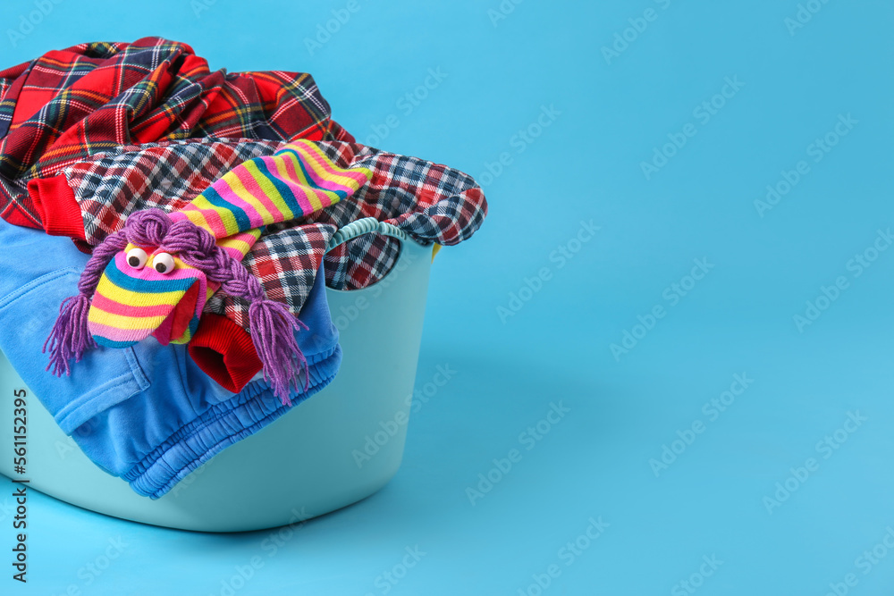 Laundry basket overfilled with child clothes on light blue background. Space for text