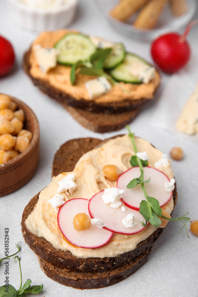 Delicious sandwiches with hummus and ingredients on light grey table