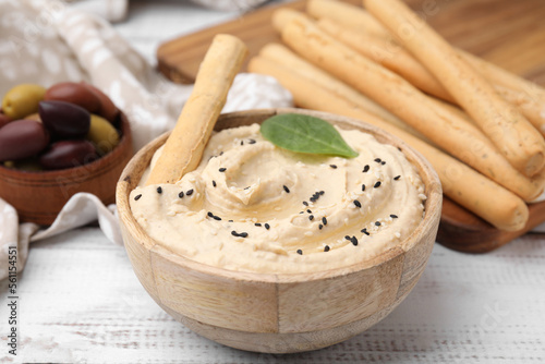 Delicious hummus with grissini stick on white wooden table, closeup