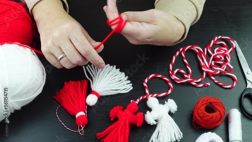 Woman making handmade traditional martisor, from red and white strings with tassel. Symbol of holiday 1 March, Martenitsa, Baba Marta, beginning of spring in Romania, Bulgaria, Moldova photo