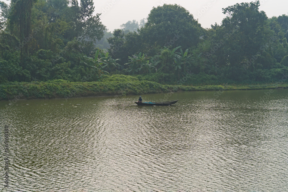 17.12.2022. An asian fisherman in search of fish in a wooden boat.