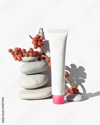 White cosmetic tube on white background. Natural minimalism, clean sustainable concept. Minimal styling still life. Beauty blogging, skin care. Mock up, flat lay, copy space. Stones, berries, shadows. photo