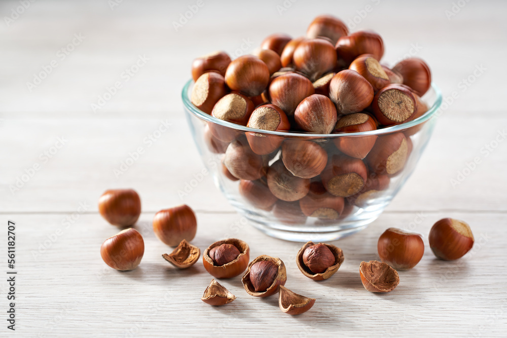 organic hazelnut in a glass plate and scattered on a white kitchen table, selective focus.