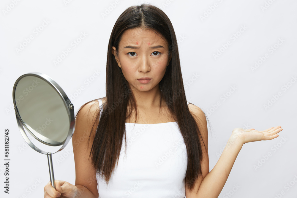 Asian woman with mirror in hand facial skin problems, acne and inflammation, red rash and allergies, chicken pox, sadness from rashes. Facial skin care concept for diseases and nerves Asian woman with mirror in hand facial skin problems, acne and inflammation, red rash and allergies, chicken pox, sadness from rashes. Facial skin care concept for diseases and nerves