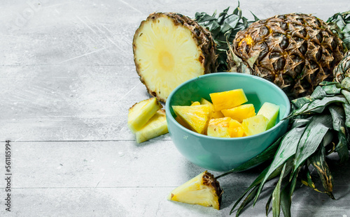Pieces of fresh pineapple in a bowl and ripe pineapples.