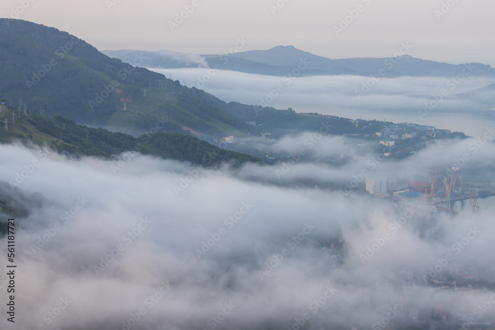 Top view of the port town on the coast of the bay. Beautiful morning landscape at dawn. Fog over the city. Avacha Bay, Pacific Ocean. Petropavlovsk-Kamchatsky city, Kamchatka Krai, Far East of Russia.