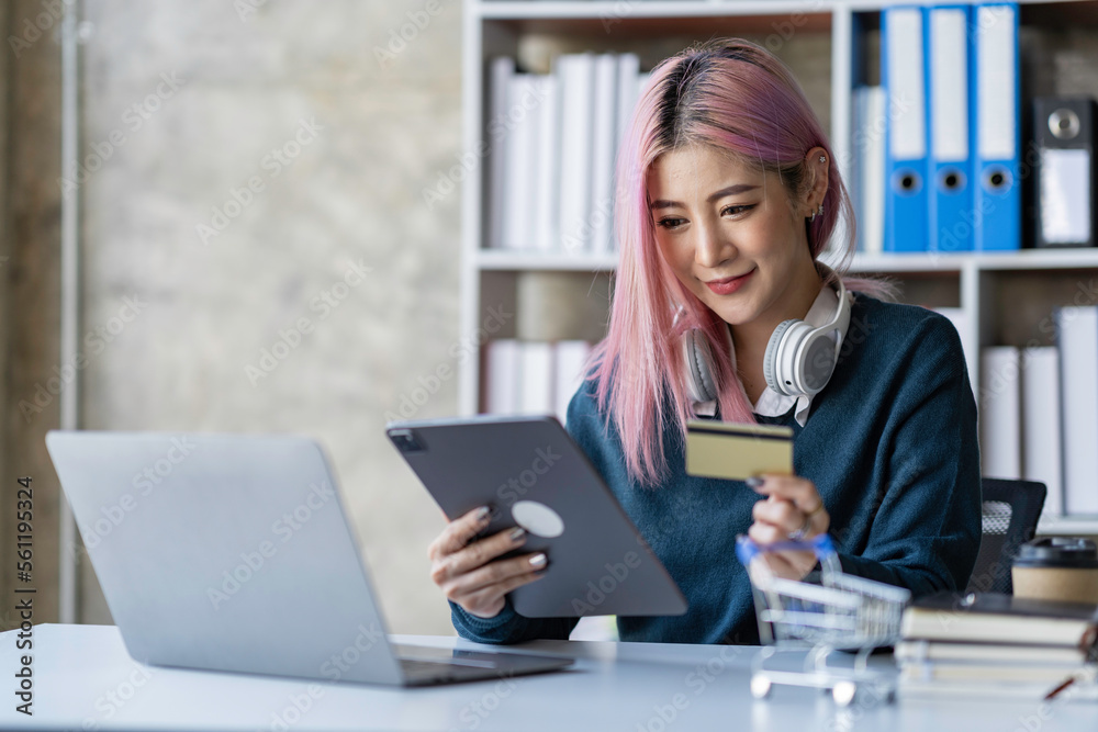 Portrait of a young Asian businesswoman enjoying online shopping with credit card payments. on laptops and tablets at the office Portrait of a young Asian businesswoman enjoying online shopping with credit card payments. on laptops and tablets at the office