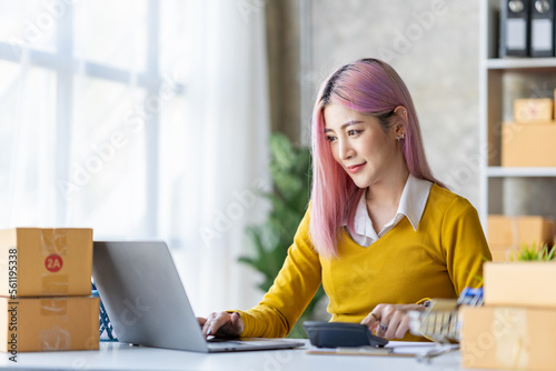 Portrait of a young Asian businesswoman sitting at a desk in an office recording data on a laptop. financial calculation and online delivery orders.