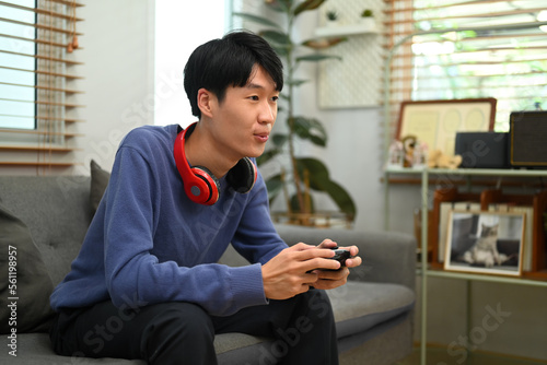 Happy young asian man player holding gamepad controller playing video game in living room