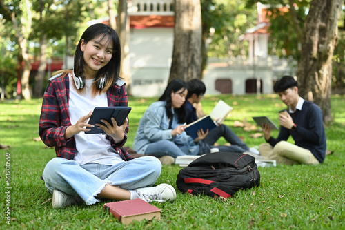 Cheerful asian student woman using digital tablet on green meadow in campus. Education, youth and community concept