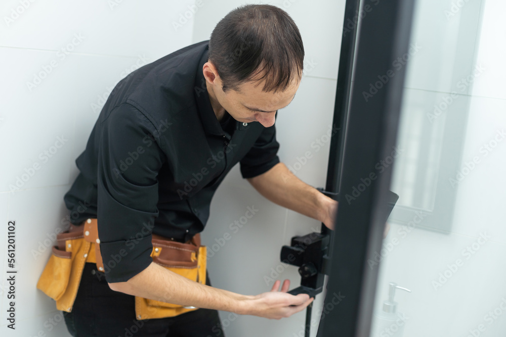 The worker is connecting the glass walls of the shower enclosure with a metal bar. The worker is connecting the glass walls of the shower enclosure with a metal bar.
