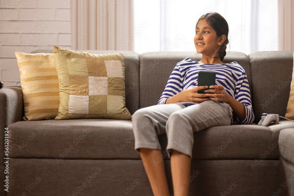 Girl using mobile phone while leaning on sofa in living room Girl using mobile phone while leaning on sofa in living room