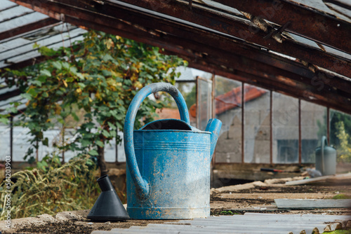 un vieil arrosoir bleu dans une serre abandonnée Un ancien arrosoir en métal bleu dans une serre horticole abandonnée. Un jardin abandonnée