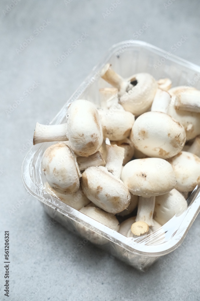 Champignon mushrooms in the plastic box at the grey background Champignon mushrooms in the plastic box at the grey background