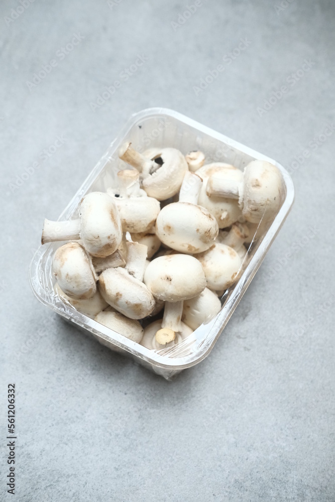 Champignon mushrooms in the plastic box at the grey background Champignon mushrooms in the plastic box at the grey background