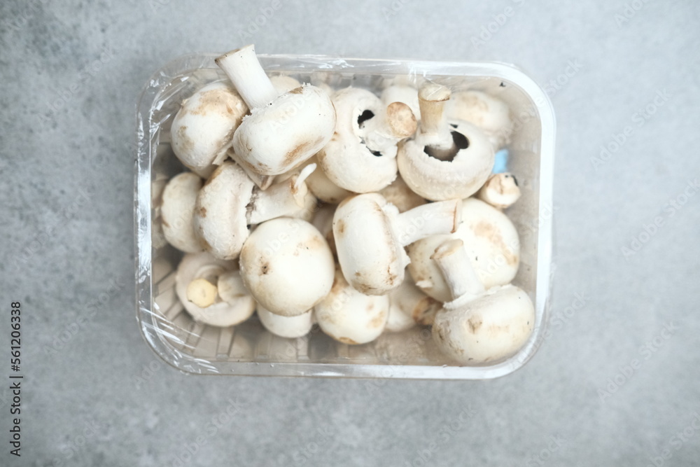Champignon mushrooms in the plastic box at the grey background	