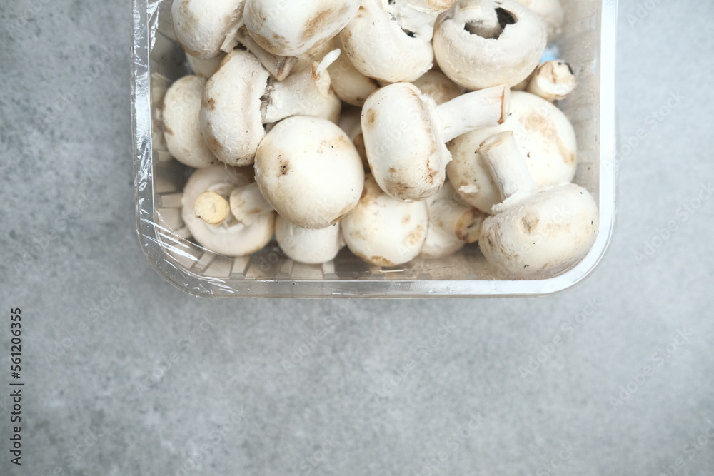 Champignon mushrooms in the plastic box at the grey background Champignon mushrooms in the plastic box at the grey background