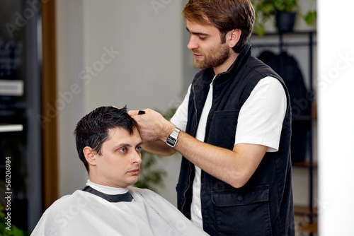 young caucasian man getting haircut by professional male hairstylist