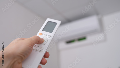 Woman hand holds remote control pointing at air conditioner in room