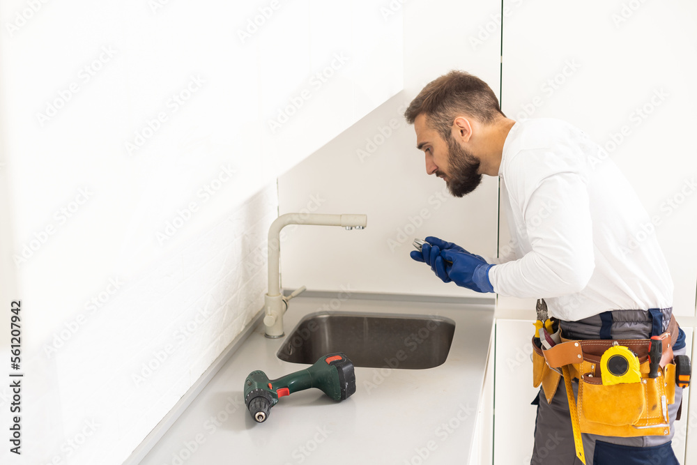 Young Repairman Installing Faucet Of Kitchen Sink In Kitchen Room Young Repairman Installing Faucet Of Kitchen Sink In Kitchen Room