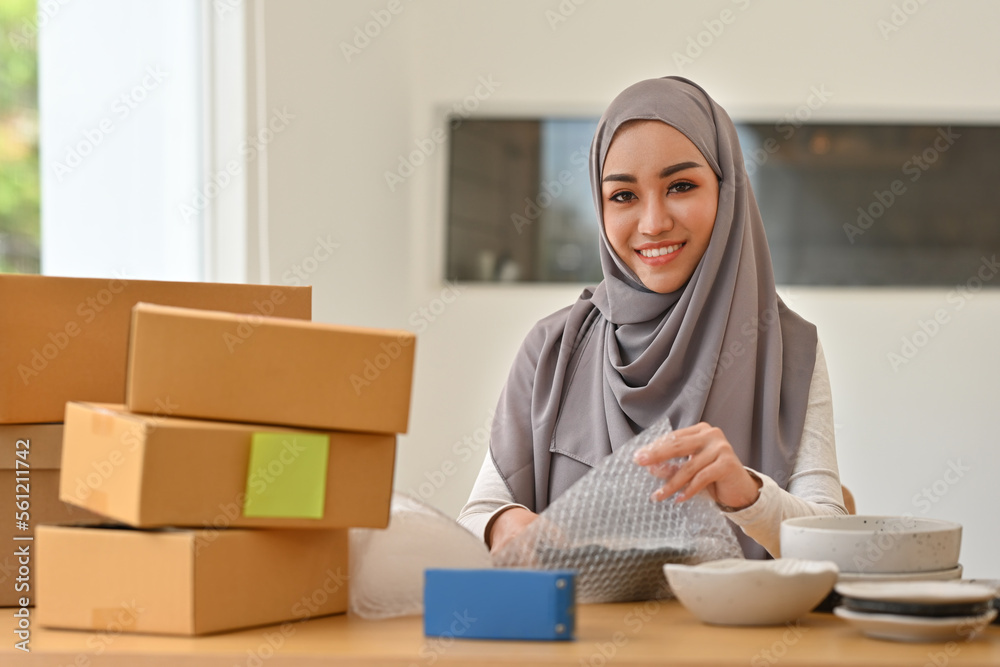Happy Arab businesswoman packing parcels to deliver to customers, Sell products online, Drop ship, SME and Delivery concept. Happy Arab businesswoman packing parcels to deliver to customers, Sell products online, Drop ship, SME and Delivery concept.