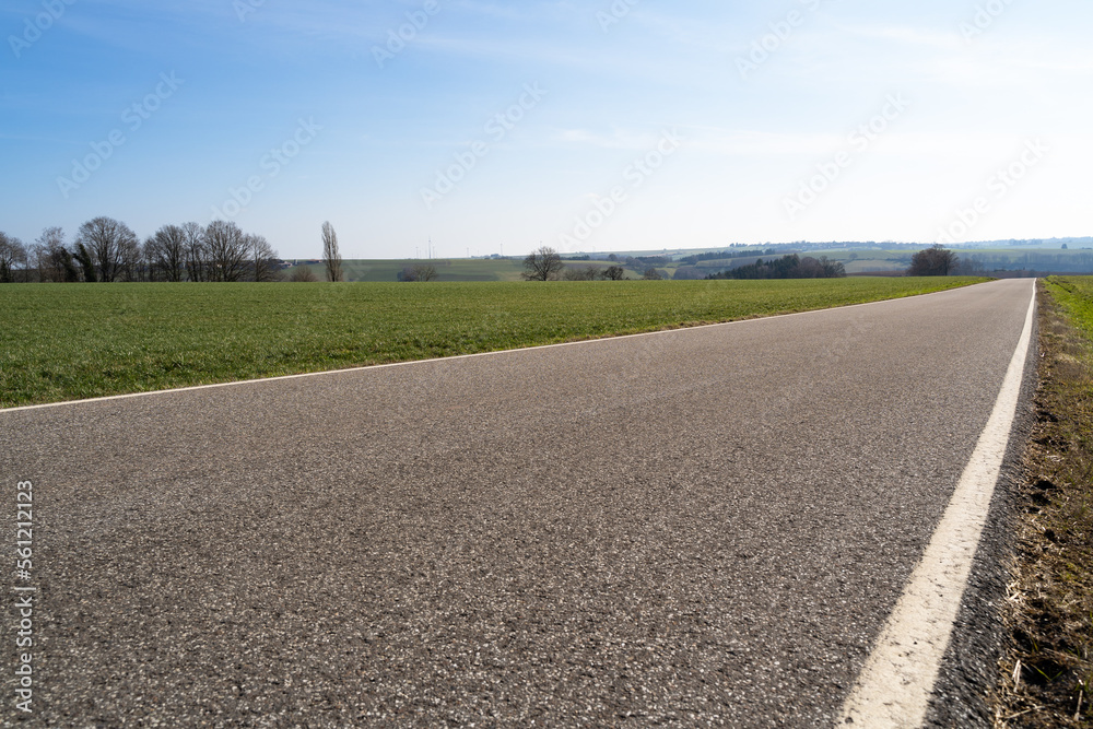 Low angle view of a paved rural road between grassfields in the landscape with blue sunny sky in spring