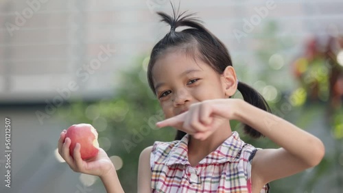 A cute Asian Thai kid girl aged 6 to 8 years old, looks healthy, holding an apple in her hand. She is eating apples. she likes to eat fruit Make her grow and be healthy. She happily eats apples. photo