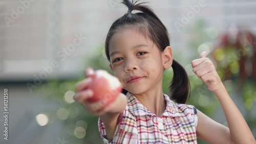 A cute Asian Thai kid girl aged 6 to 8 years old, looks healthy, holding an apple in her hand. She is eating apples. she likes to eat fruit Make her grow and be healthy. She happily eats apples. photo