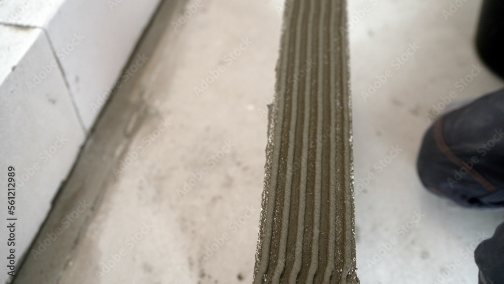 The adhesive solution is applied to the floor. Master husband presses a spatula glutinous solution to the cement surface. The adhesive solution is applied to the floor. Master husband presses a spatula glutinous solution to the cement surface.