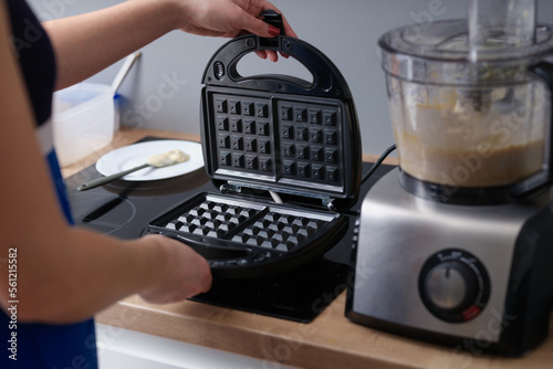 Woman opens waffle iron to make waffles in kitchen.